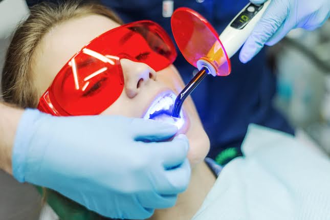 Dentist performing dental filling treatment using blue light curing on patient wearing protective glasses in dental clinic